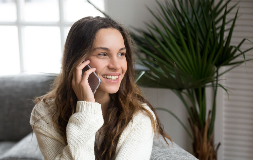 Photo of a smiling woman sitting on her sofa on the phone