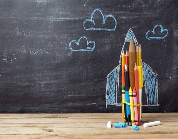 Image showing a school blackboard with a rocket drawn on and some pencils and crayons in front of it